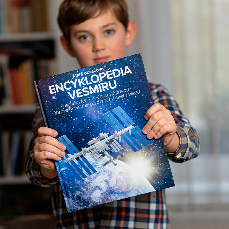 Kniha Encyklopedie vesmíru. Chlapec drží knihu v ruce před sebou. Náš je design obalu knihy.